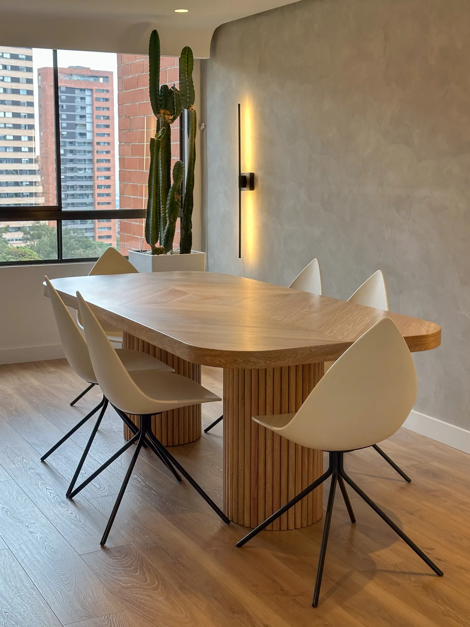 La Campiña W&D – Comedor con mesa de madera de bordes curvos y muro en estuco